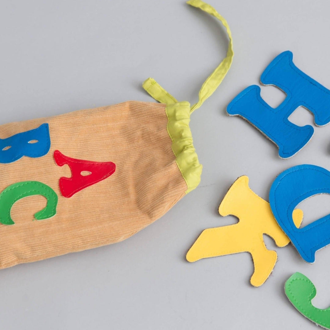 Colorful fabric alphabet letters scattered around canvas storage bag on wooden surface showing tactile learning toy