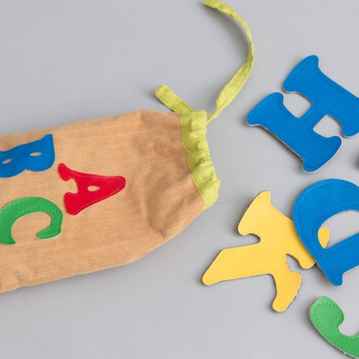 Colorful fabric alphabet letters scattered around canvas storage bag on wooden surface showing tactile learning toy