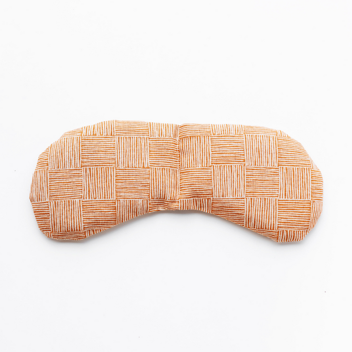Weighted eye mask with checkered orange pattern for migraine relief and tension reduction.