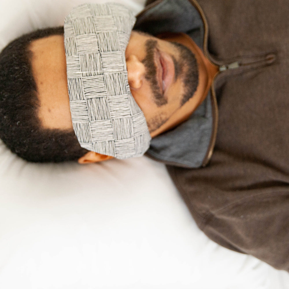 Man relaxing with weighted eye mask featuring neutral textural pattern for migraine relief and stress reduction.