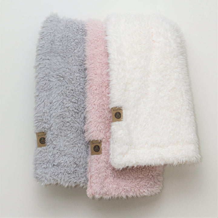 Three Angel Plush blankets in Silver, Pink, and Whisper White, showcasing their fluffy texture and luxurious softness. Perfect for cozy interiors.