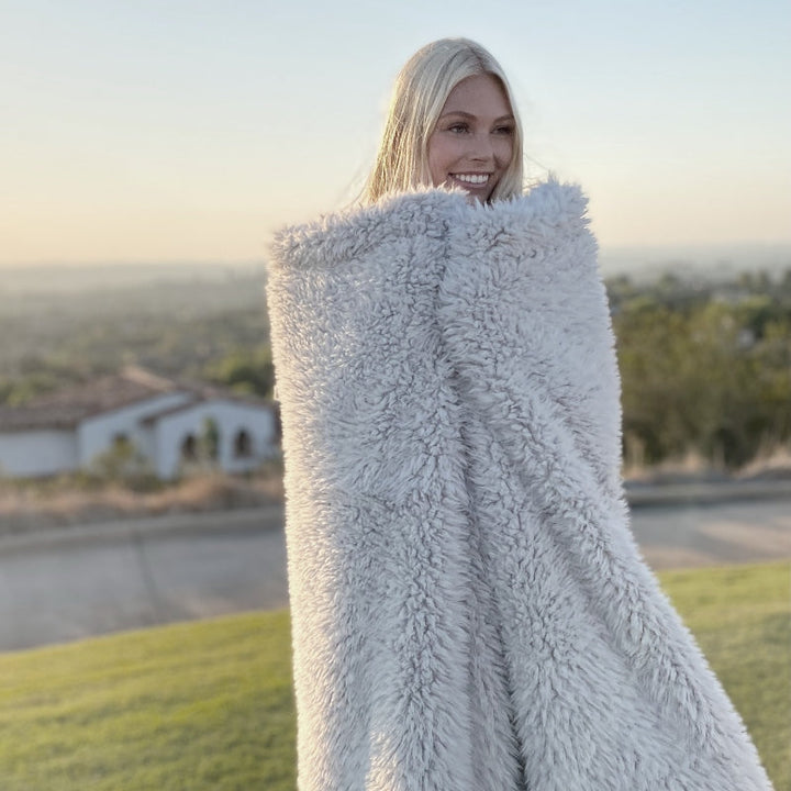 Woman wrapped in soft Angel Plush blanket standing outdoors, showcasing its sumptuous softness and calming neutral color.