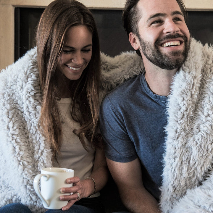 Couple enjoying a cozy moment with a plush blanket, woman holding a mug, the Angel Plush Blanket draped over their shoulders.