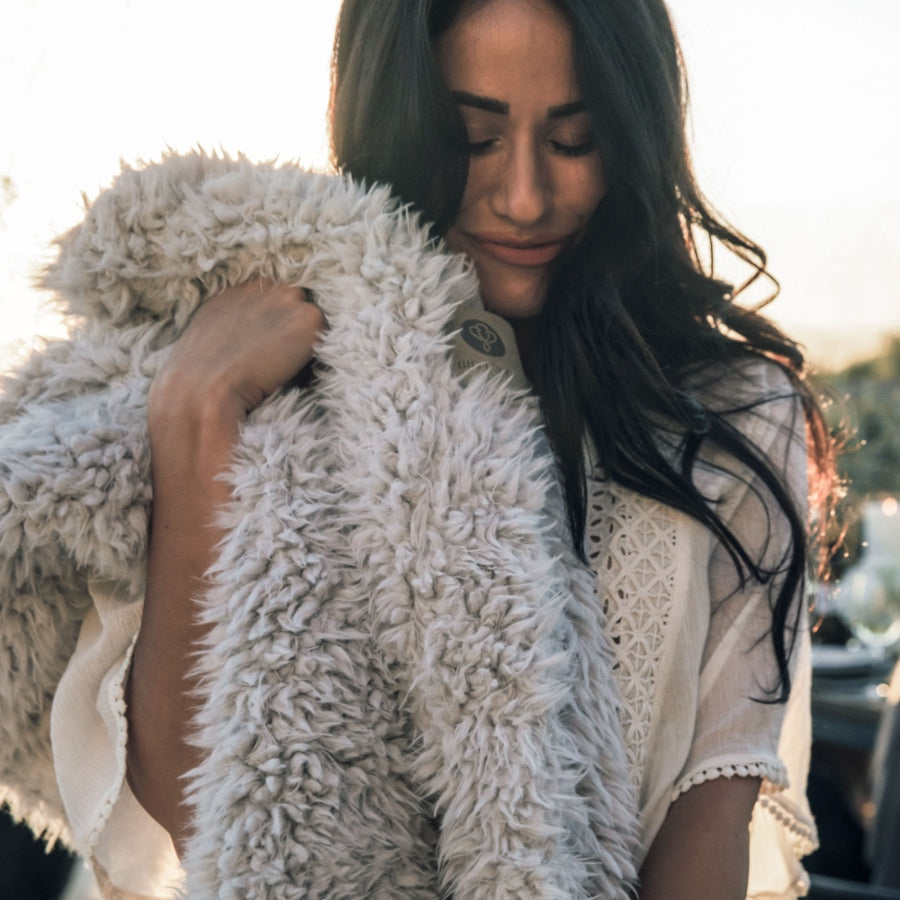 Woman enjoying the softness of an Angel Plush blanket in Silver tones, perfect for any home. Light and luxurious comfort.