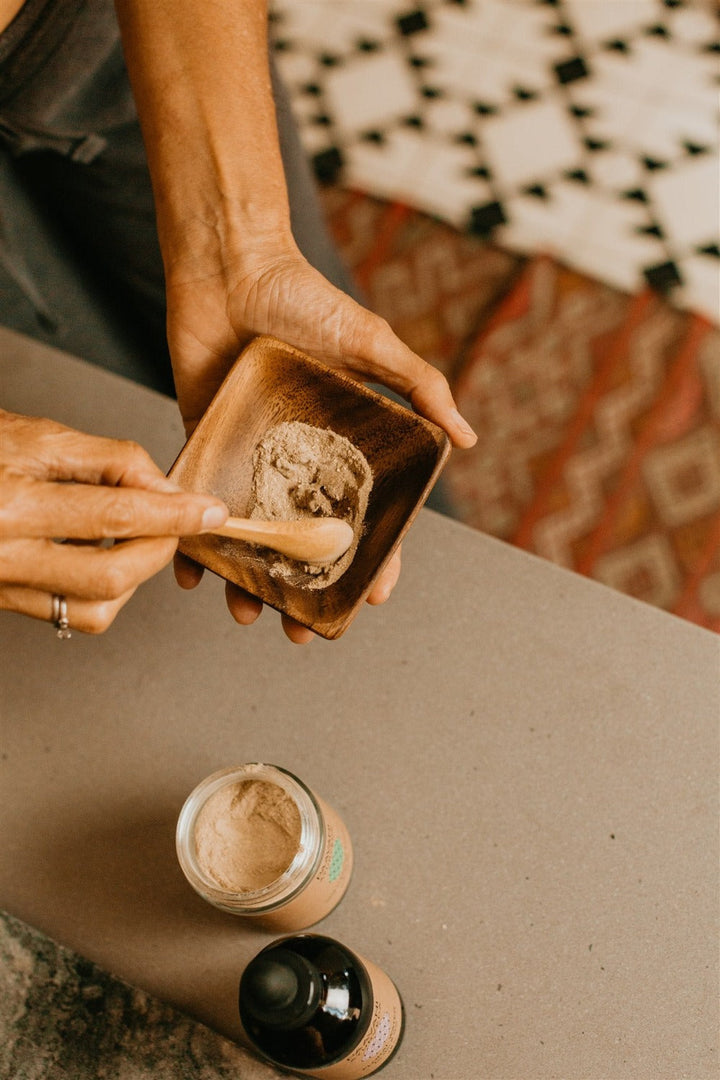 Person using The Pitta Skincare Ritual Ayurvedic products for sensitive skin care routine with powder in wooden bowl and jars.