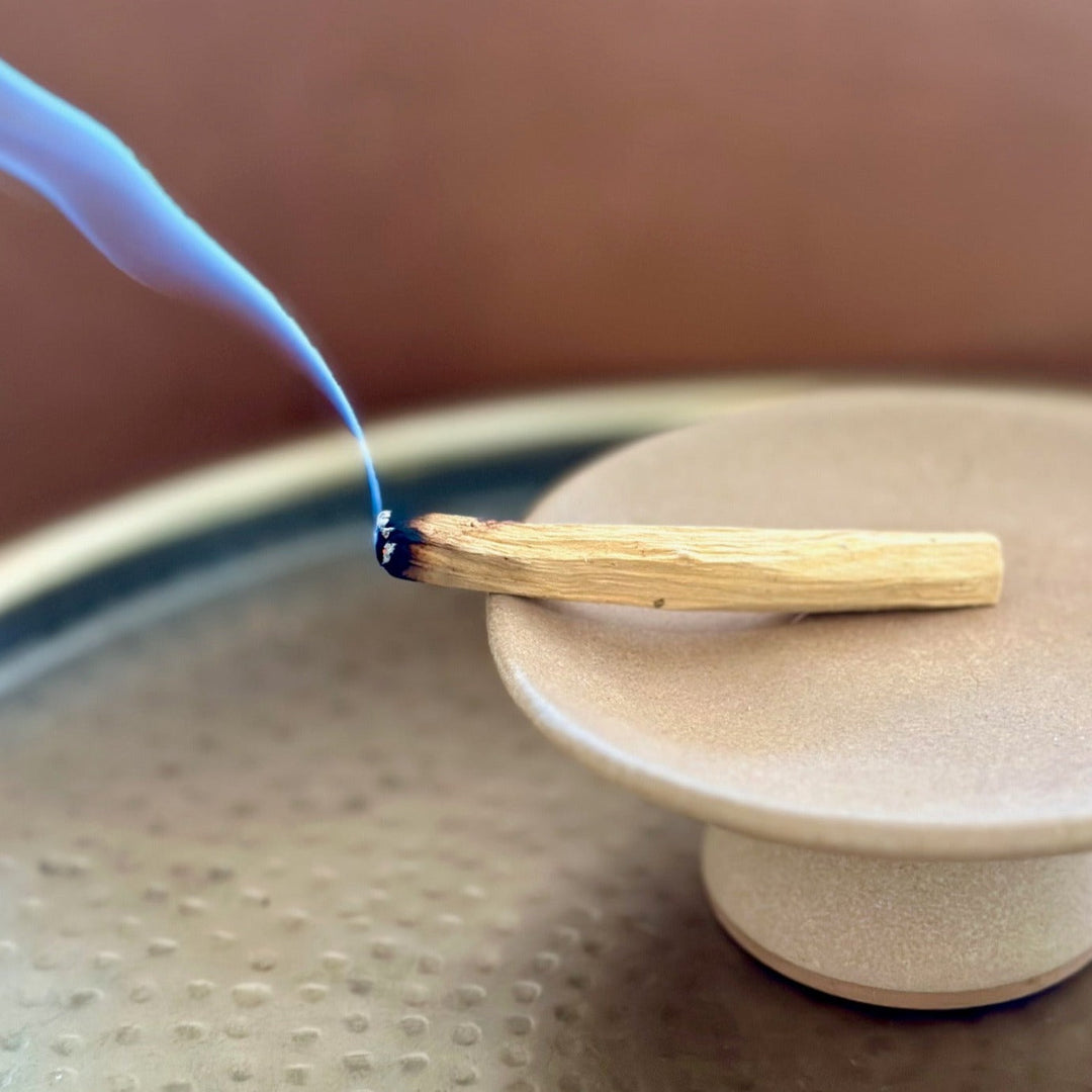 Eco-friendly Palo Santo incense stick burning with blue smoke on a ceramic holder, offering an aromatic and spiritual experience.
