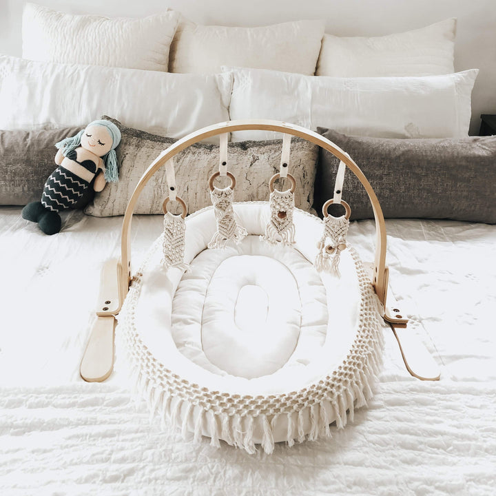 Organic cotton oval baby play mat with macrame fringe in boho nursery setting for infant floor play