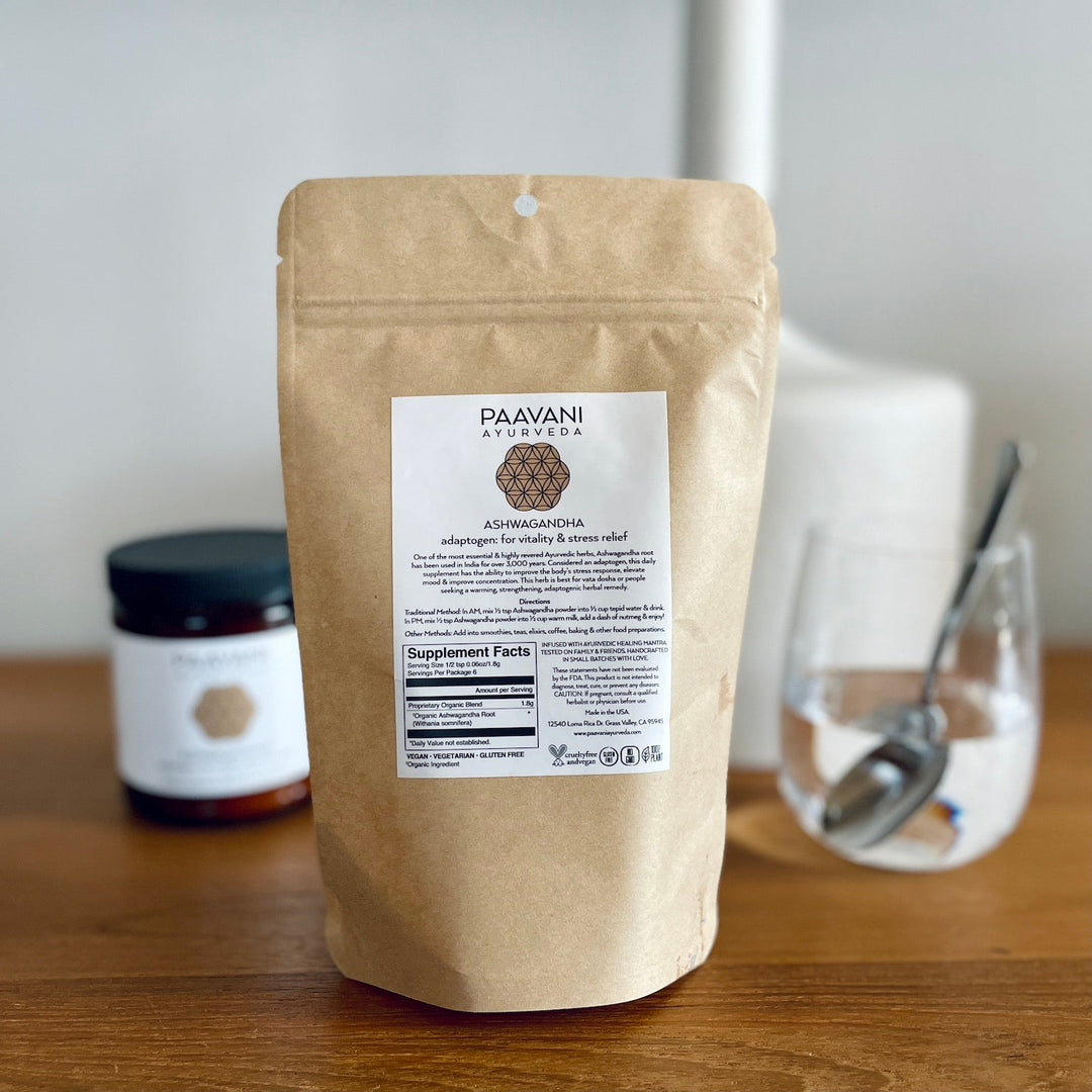 Ashwagandha Powder by Paavani Ayurveda in compostable refill bag on a table with a jar and spoon. For stress relief and mood enhancement.
