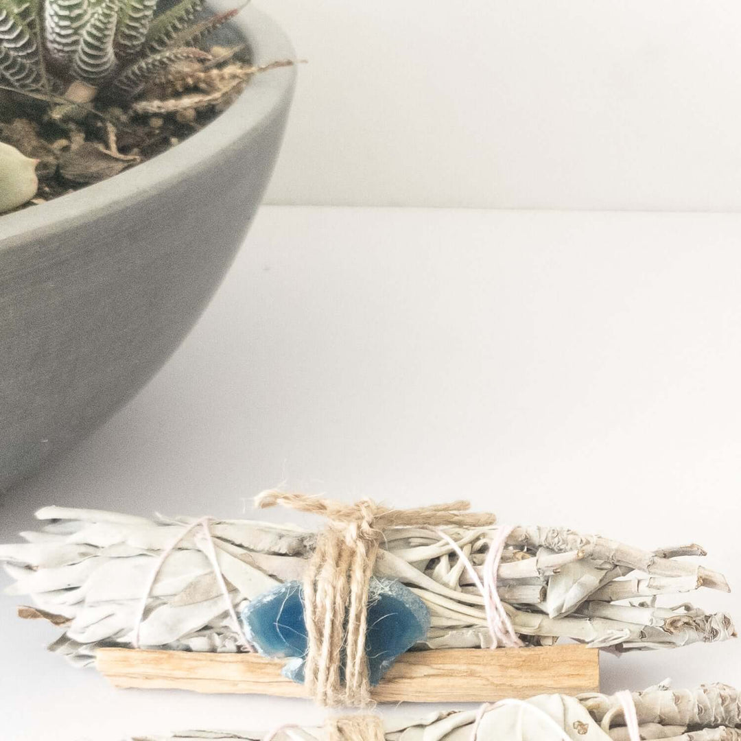 Palo Santo, crystal, and sage smudge bundle for spiritual cleansing with nature plant in background.