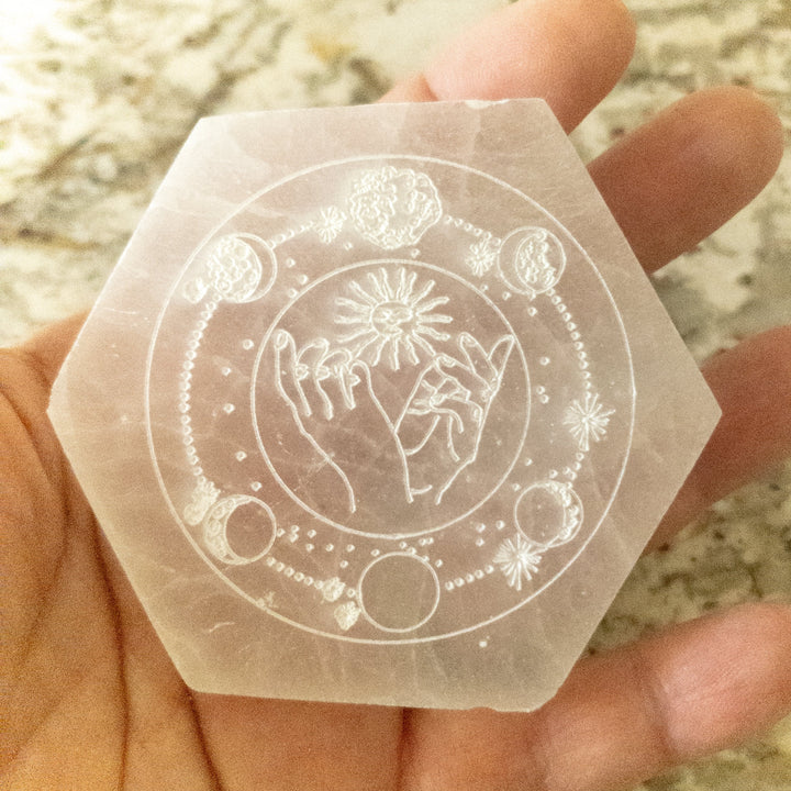 Engraved selenite hexagon plate with celestial sun and moon phases design on white crystal surface
