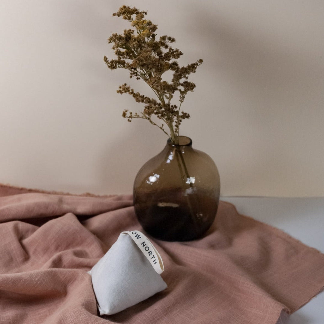 Lavender sachet on fabric beside a vase, ideal for freshening clothes, drawers, and cars with calming aroma.