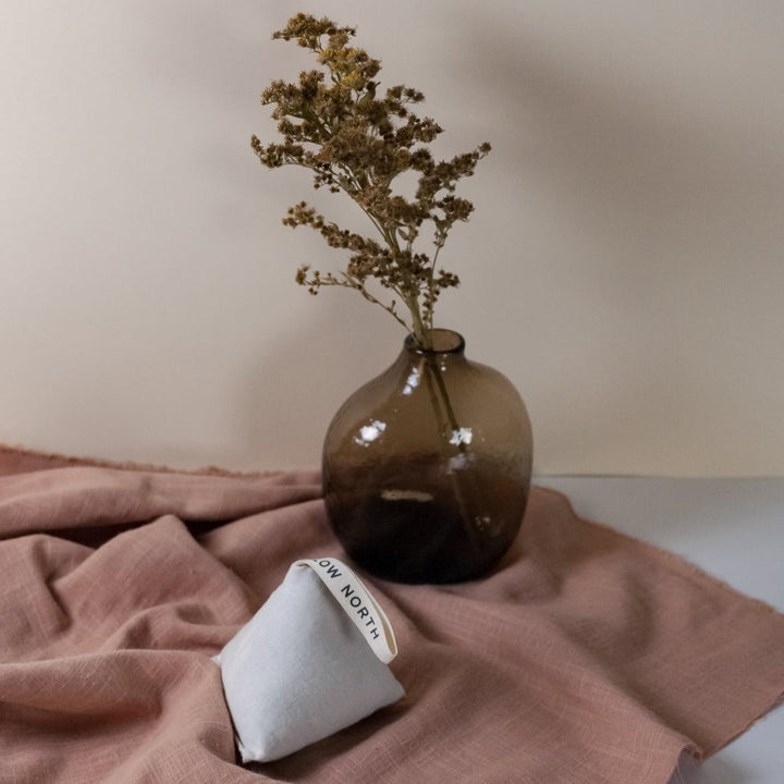 Lavender sachet on fabric beside a vase, ideal for freshening clothes, drawers, and cars with calming aroma.