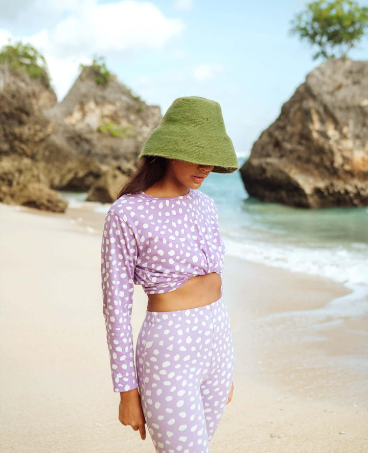 Woman wearing Naomi Jute Clochet Straw Hat in Matcha Green on a sunny beach day, showcasing its wide brim and stylish design.