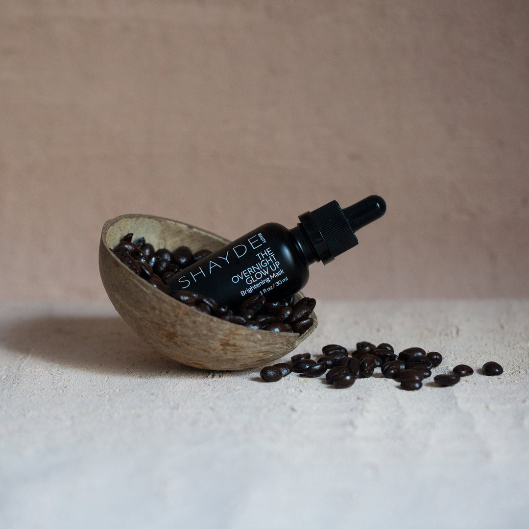Overnight Glow Up Mask bottle in a coconut shell with coffee beans, featuring award-winning skincare formula.