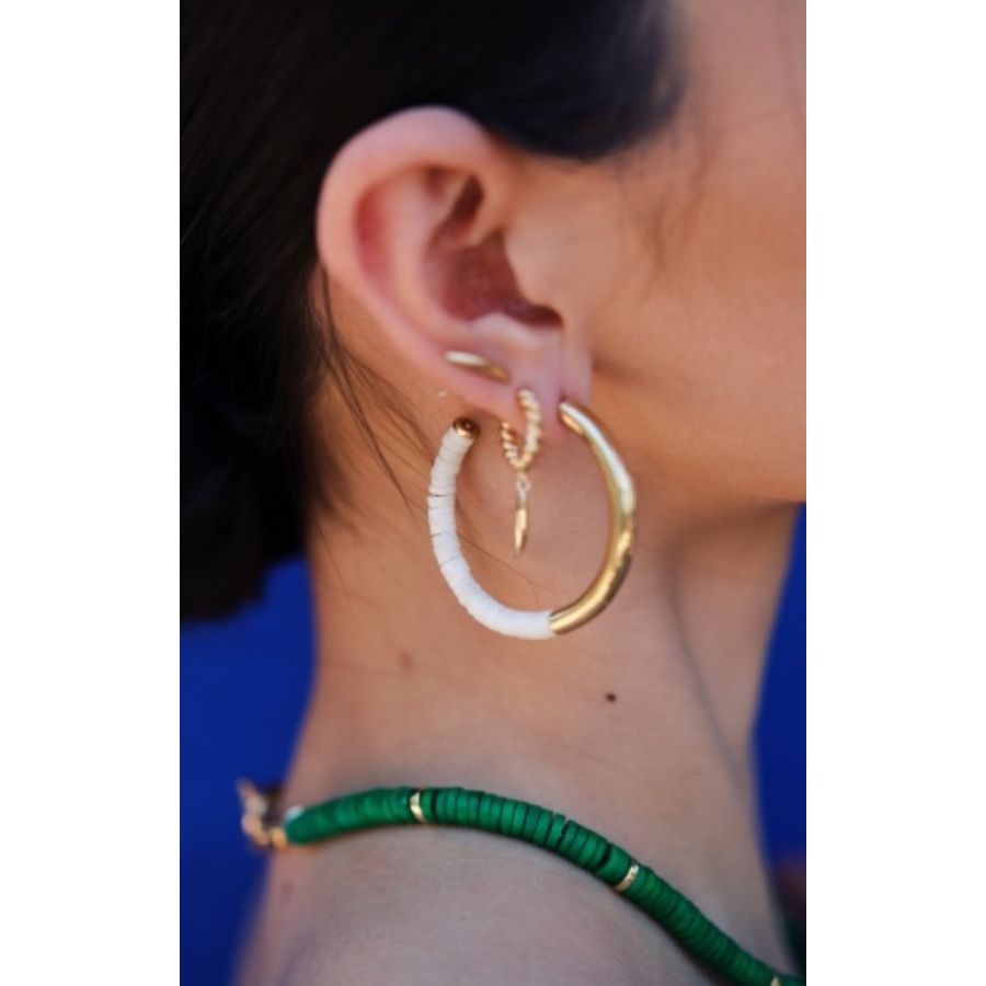 Close-up of a woman wearing Capped Quill Minimalist Dangle Earrings with a green necklace against a blue background.