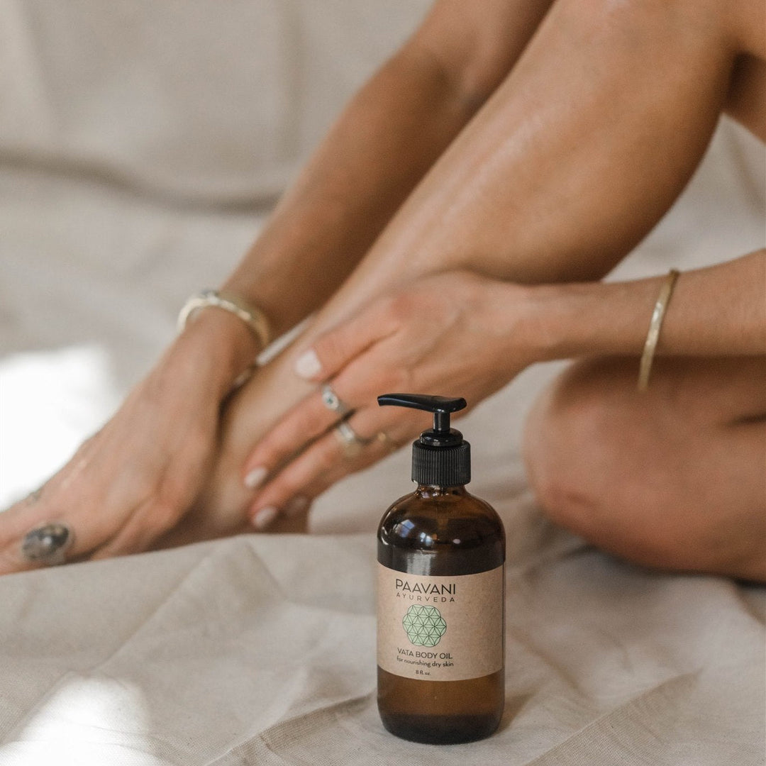 Bottle of Vata Body Oil for dry skin with person applying it to feet, promoting ayurvedic skincare and hydration.