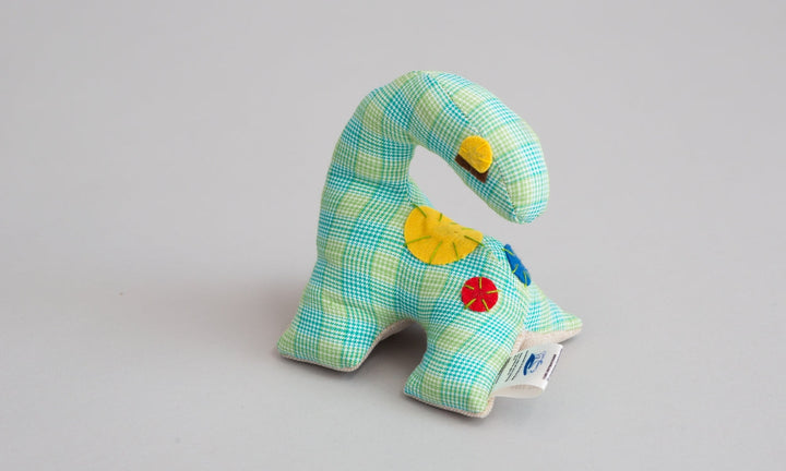 Small handmade green plaid dinosaur plush toy made with fleece and felt sitting upright showing textured materials