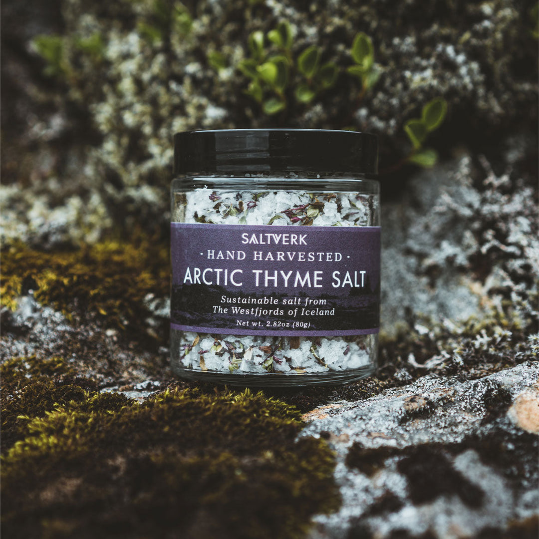 Jar of hand-harvested Arctic Thyme Salt from Iceland, placed on mossy rocks, representing sustainable sub-Arctic flavor.