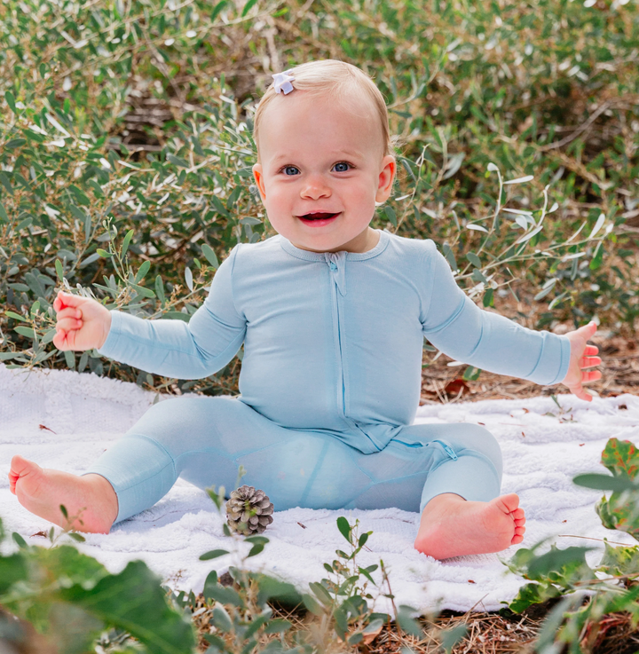 Baby wearing Luxe Bamboo Baby Pajamas in Blue, sitting outdoors on a blanket, showcasing comfort and softness of the fabric.