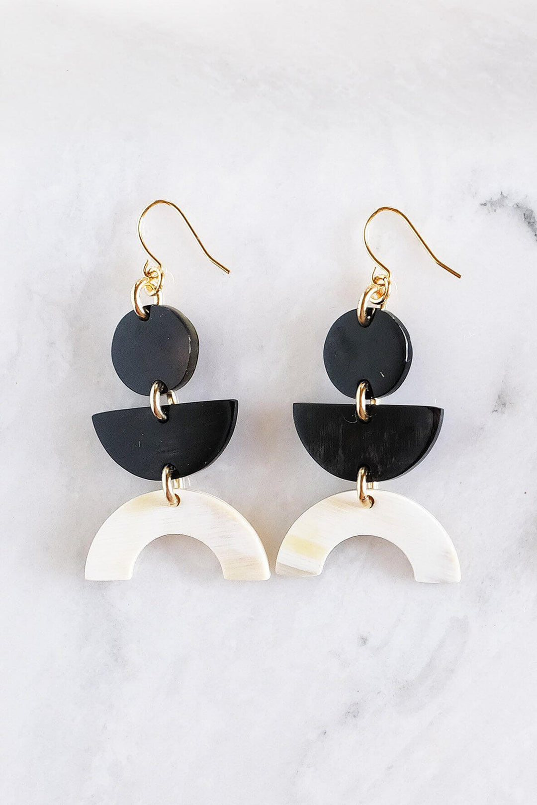 Vui Mung geometric buffalo horn earrings in light and dark horn with gold-plated hooks, handcrafted and chemical-free, displayed on a marble surface.