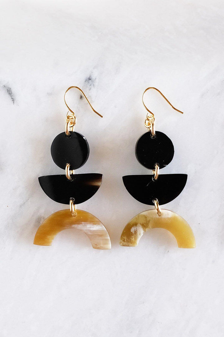 Vui Mung geometric buffalo horn statement earrings in dark and honey horn with gold-plated hooks against a marble background.