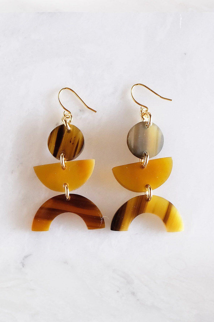 Vui Mung geometric buffalo horn statement earrings in honey horn with gold-plated hooks on a marble background, handcrafted and eco-friendly.