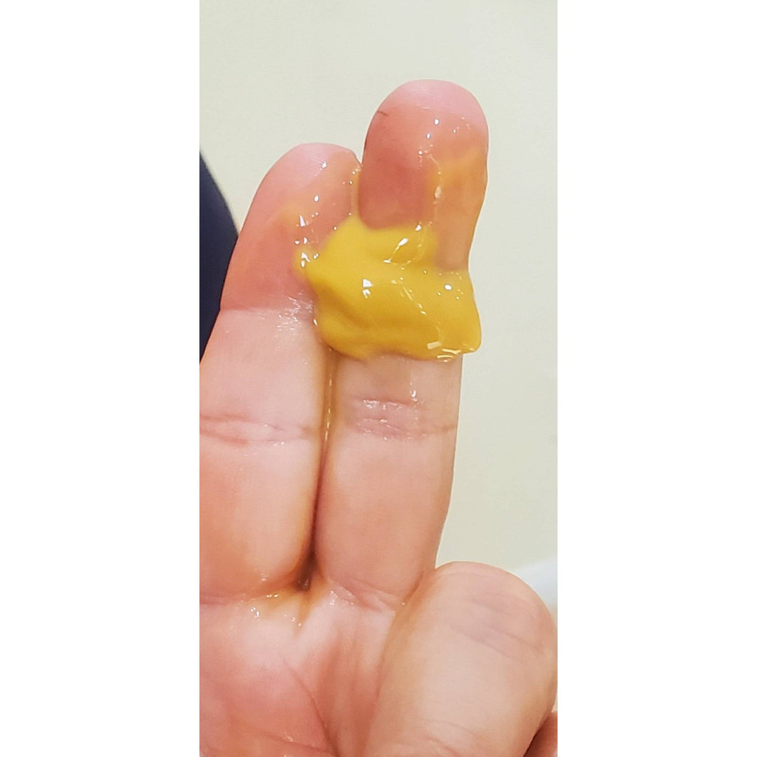 Close-up of fingers with a smear of yellow Bakuchiol serum, demonstrating texture and consistency of this plant-based retinol alternative.