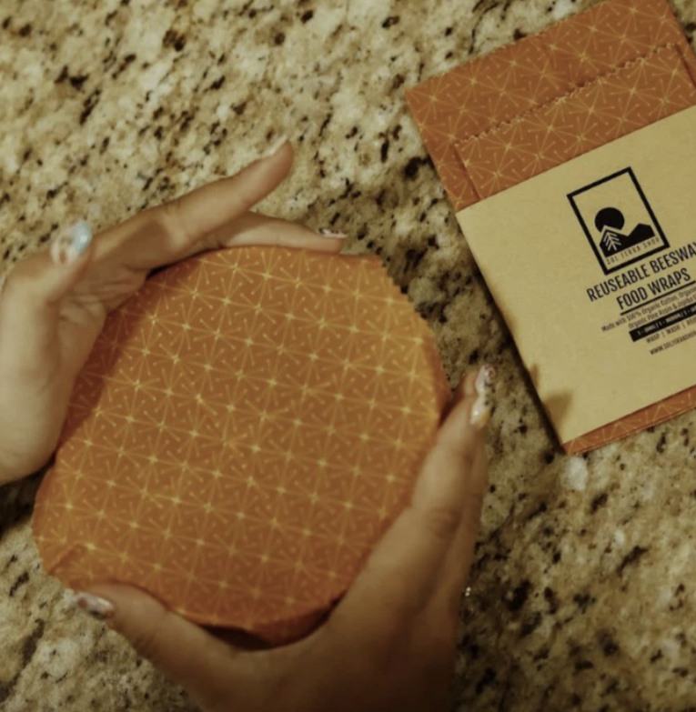 Hands holding reusable beeswax food wrap on granite surface, eco-friendly alternative to plastic wrap, with packaging beside.