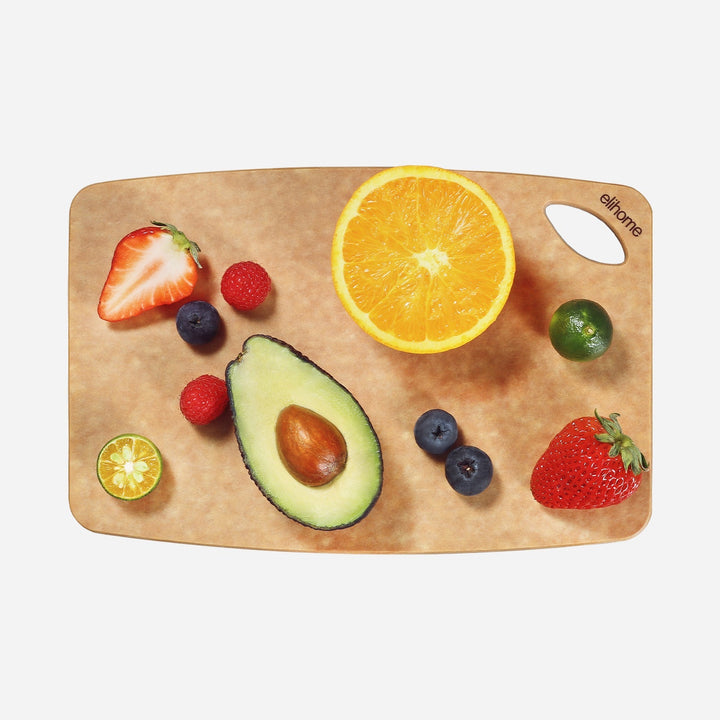 Small reversible cutting board with thumb hole on white surface next to fresh vegetables