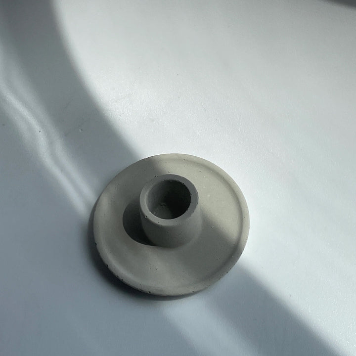 Handmade concrete candle holder for standard taper candles, 2.5cm, minimalist design, made in Canada, casting shadows on white surface.