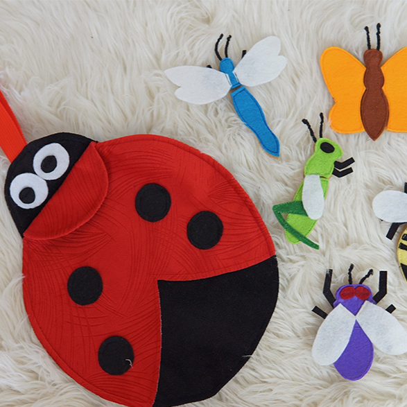 Colorful fabric flying bugs assembly kit with butterfly, dragonfly, and other insect pieces on rollable play mat