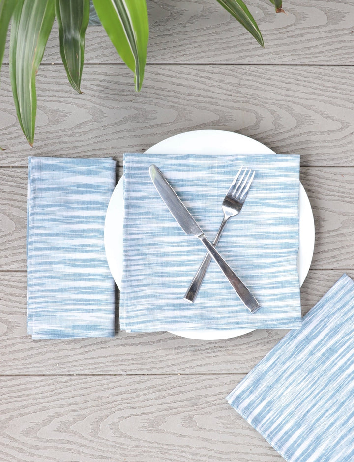 Light blue handwoven cotton dinner napkins folded on natural linen table setting with ceramic plates