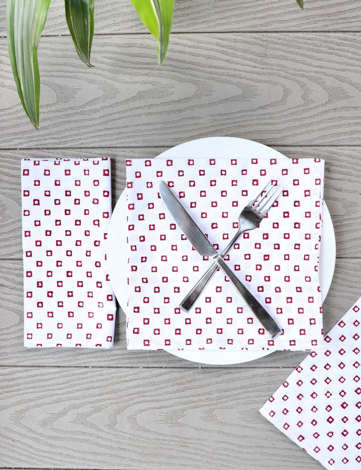 Red square cloth napkins handmade from cotton with block print pattern, set of four folded napkins on table