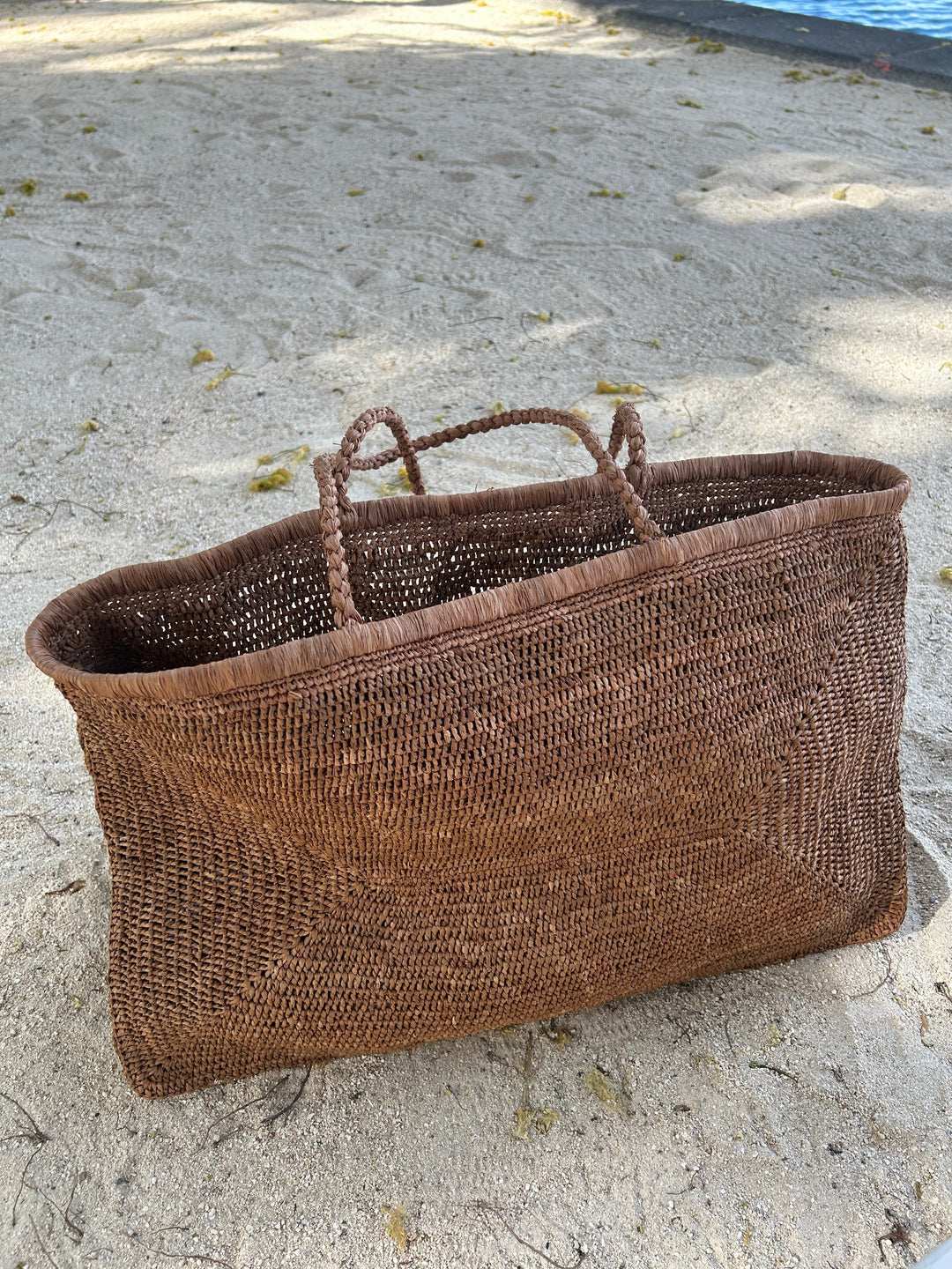 Handmade raffia beach tote bag on sand, crafted in Madagascar, featuring durable natural fibers and artisan design, perfect for beach days.