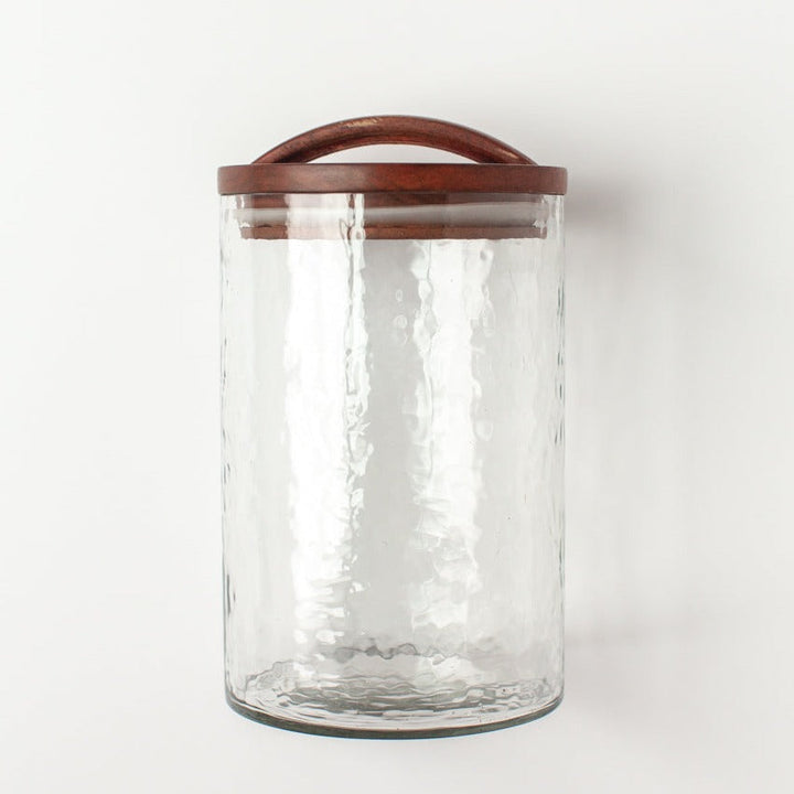 Clear glass canister with hand-carved wooden lid, ideal for kitchen storage or apothecary use. Features an airtight seal. Made in India.
