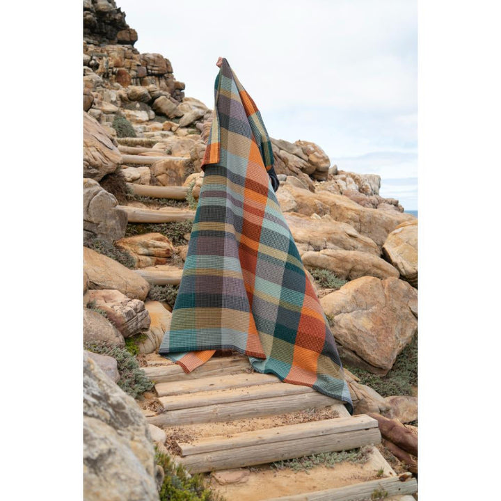 Vrou-Vrou Textured Blanket in Cypress on rocky outdoor steps, woven in South Africa from 100% cotton, adds bold, artistic flair to any space.