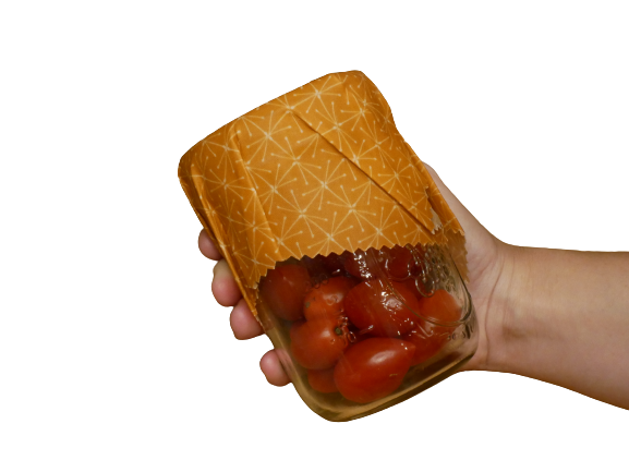 Hand holding a jar of tomatoes covered with the Orange Stars beeswax food wrap for eco-friendly food storage.