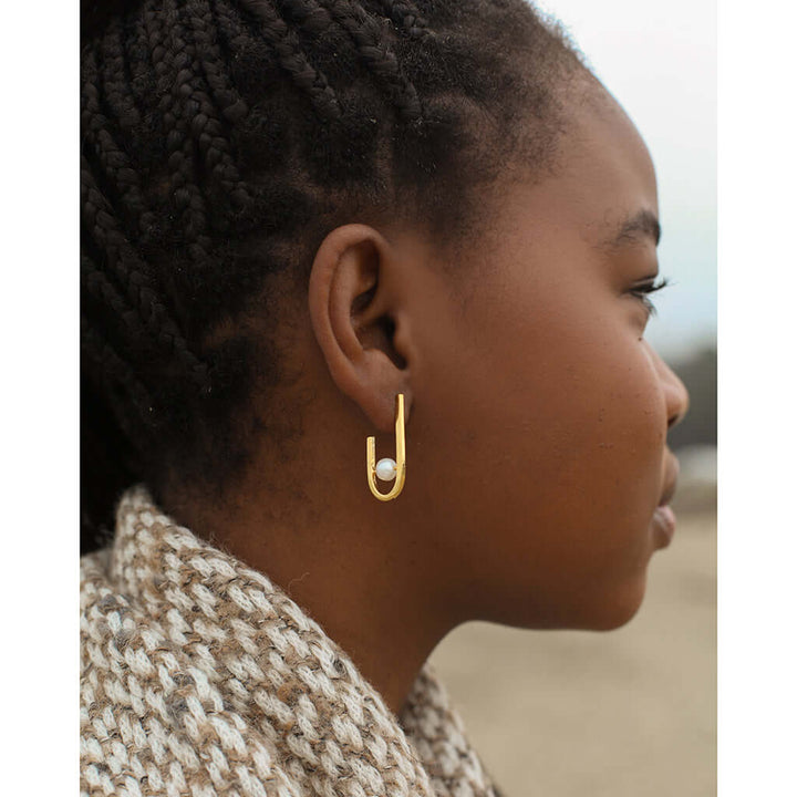 J Hoop Freshwater Pearl Earrings showcased on a woman's ear, crafted from recycled bombshells, gold plated, minimalist design.