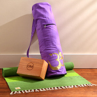 Handwoven cotton yoga mat with OM design, purple carrying bag, and wooden yoga block on hardwood floor