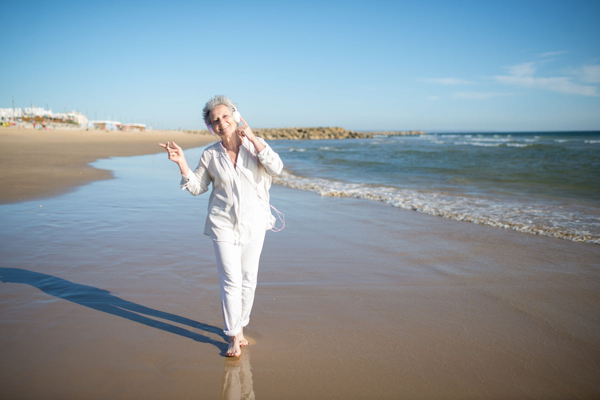 A woman dressed in white walking barefoot along the shore