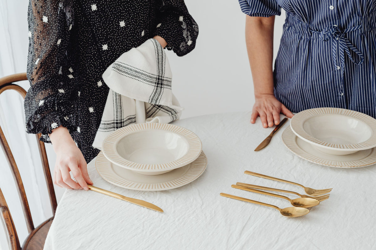 A linen table set with ceramic plates and gold cutlery