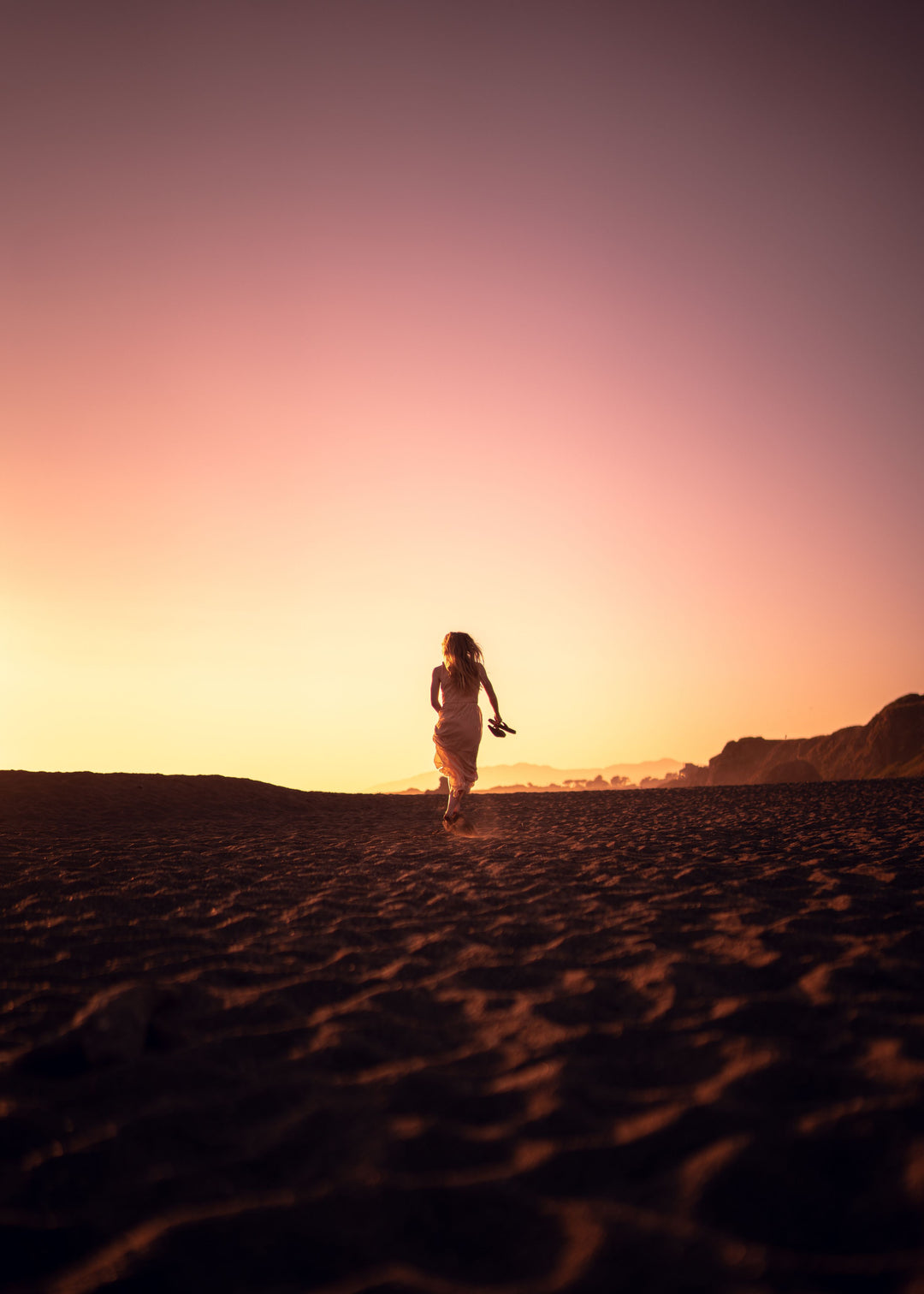A woman walking barefoot along the shore at sunset