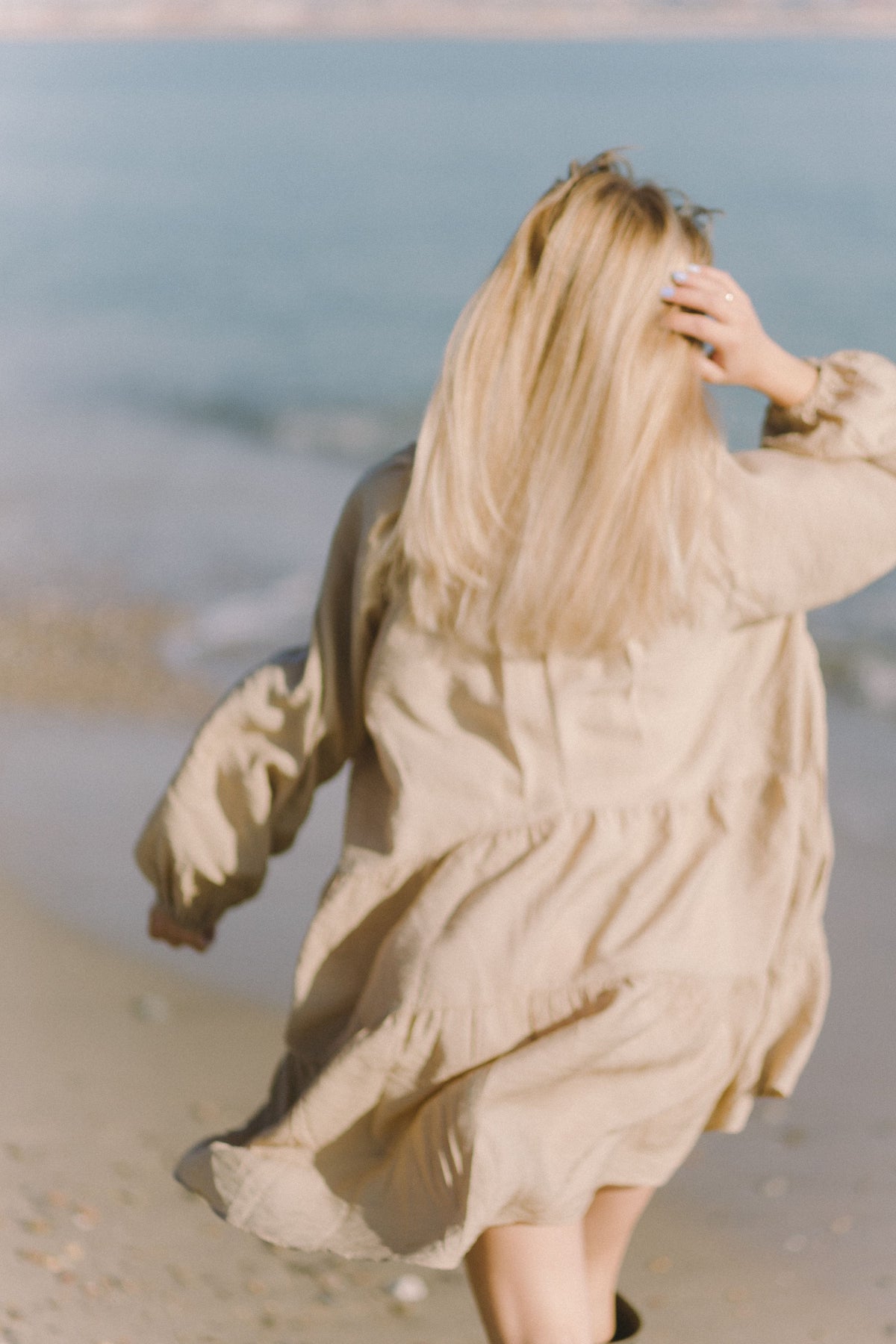 A woman in a beige dress walking on the beach